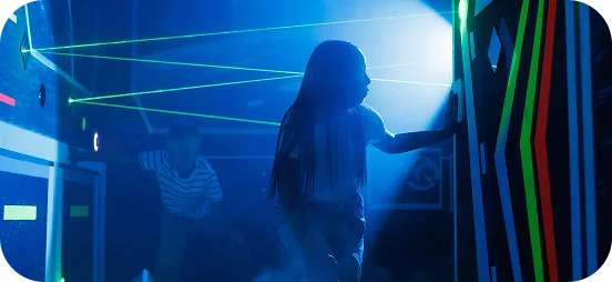 Dwoje dzieci gra w laser tag w neonowo oświetlonej arenie, wykorzystując przeszkody i strategię podczas pełnej akcji gry.